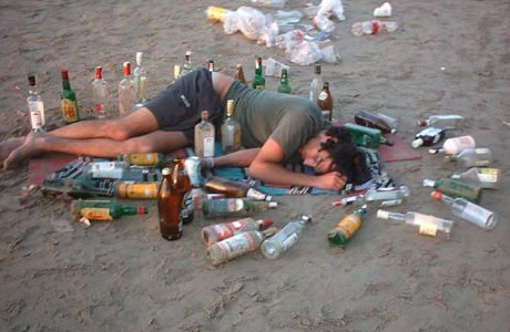 Spící člověk na zemi na pláži mezi lahvemi od alkoholu